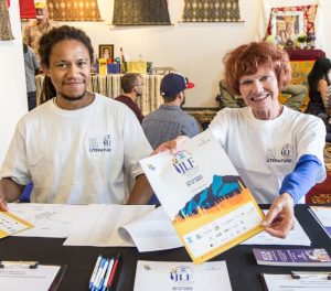 Two volunteers smiling and holding out a paper program.